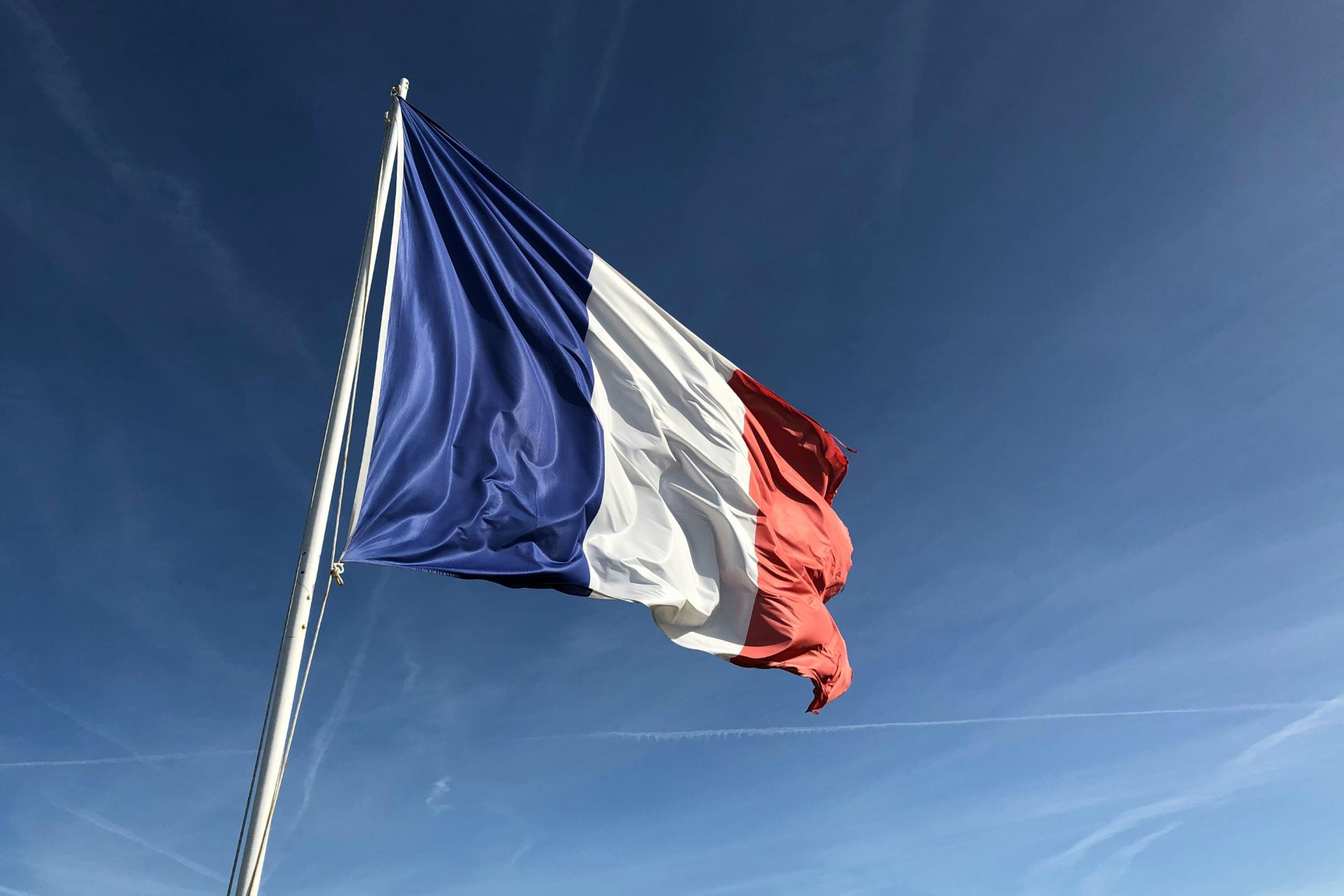 Auf dem Bild ist die französische Flagge in den Farben blau, weiß und rot vor einem blauen Himmel zu sehen